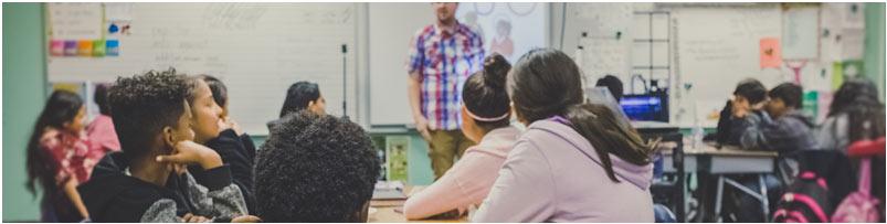 Many students sitting at desks face away from the camera, listening to a teacher who tells them what you can do with a public health degree.