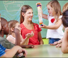 Smiling teacher stands behind two students working at their desks.