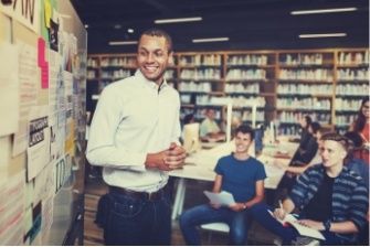 A smiling man stands at the front of a classroom teaching after learning what you can do with an education degree.