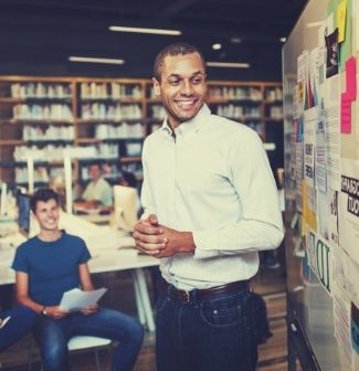 A smiling man stands at the front of a classroom teaching after learning what you can do with an education degree.