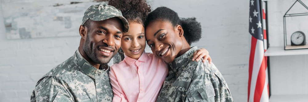 A man and woman in military uniforms holding a young girl wearing a pink shirt.