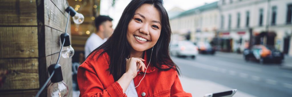 A smiling woman outside listening to something on her headphones.