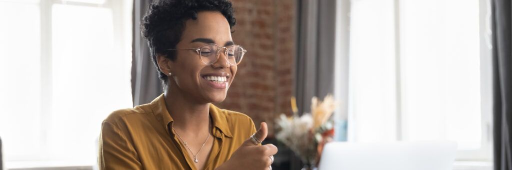 A woman sitting in front of her laptop and smiling while giving the thumbs up sign.