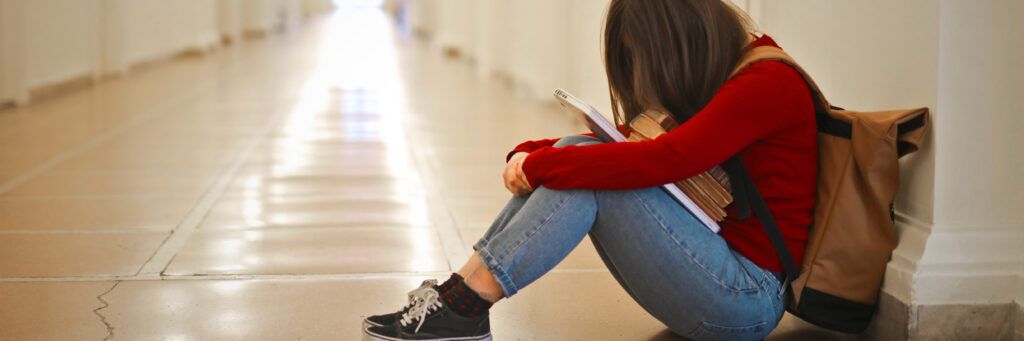 A sad female student sitting on the floor with her head down.