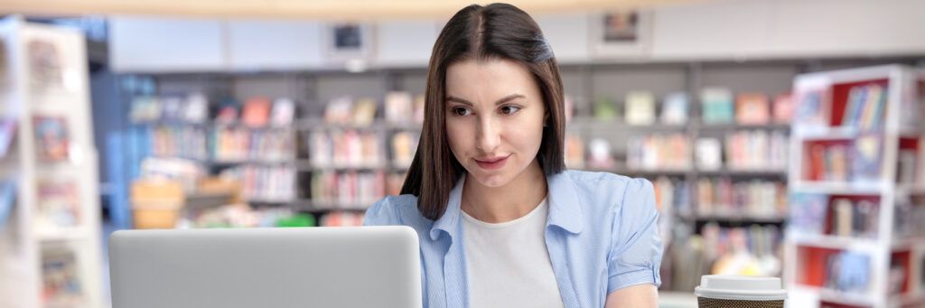 A female student sitting at a desk in the library looking at the laptop in front of her. 