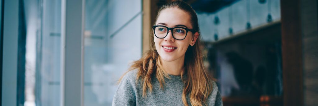 A smiling woman wearing glasses looking at something off in the distance.