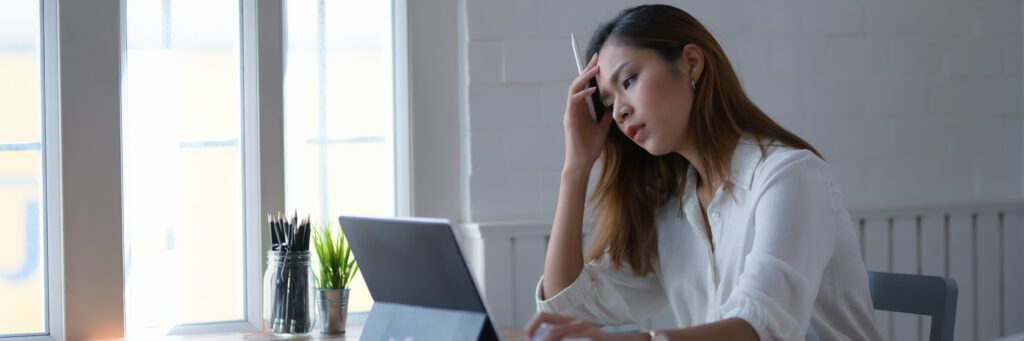 A female student at a desk concentrating on the work she’s doing on her laptop while holding a pen in her hand.