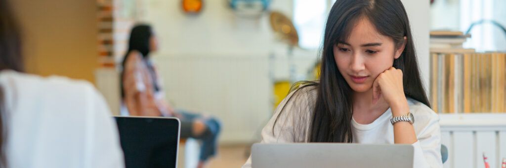 A female student sitting at a desk in the library looking at her laptop.