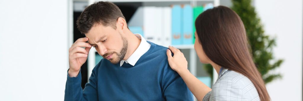 A woman putting her hand on a distraught man’s shoulder to comfort him.