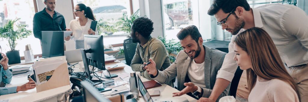 A diverse group of people sitting at a table with their computers while collaborating together.