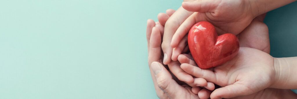 A group of hands holding a red stone heart.