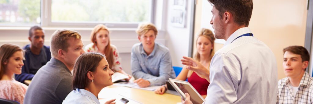 Male teaching professor addressing a group of student teachers in a classroom.