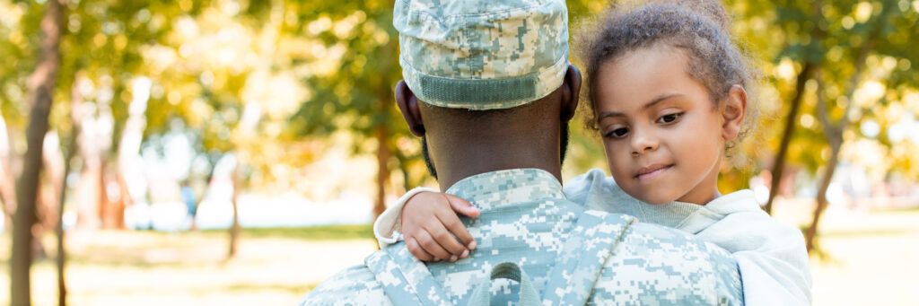 Man in military holding his daughter, who is smiling.