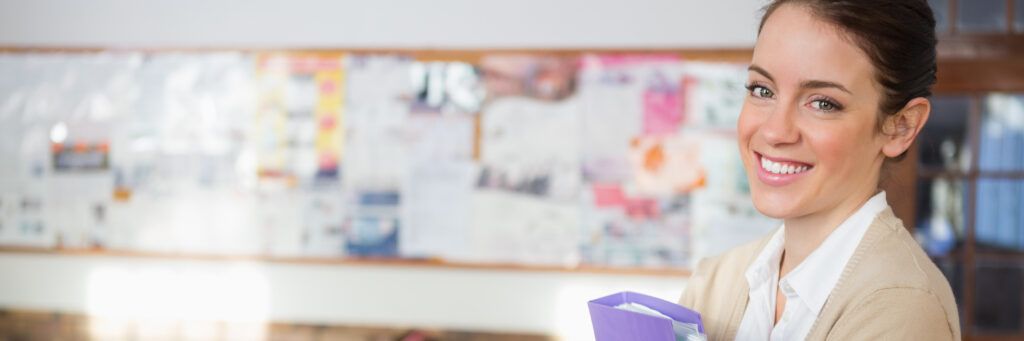 Female student with purple binder smiling in a classroom.