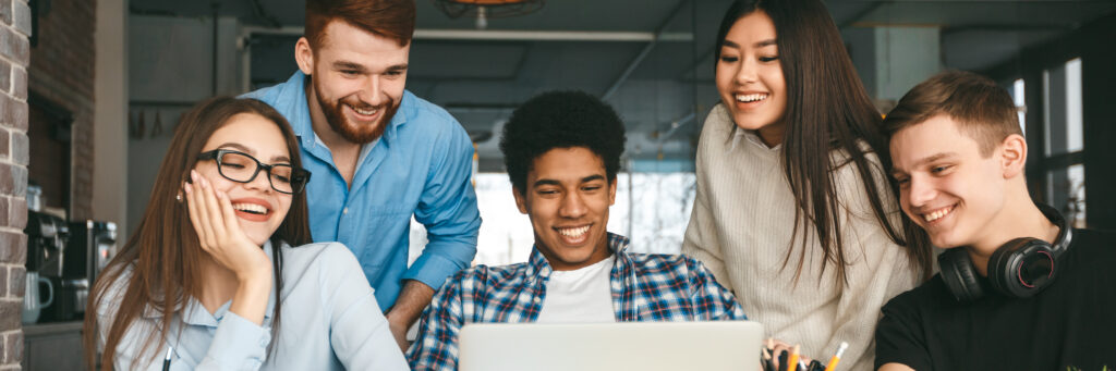 Five college students smiling at the FAFSA application on a laptop.