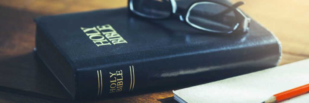 The bible laying on a table with a pair of glasses on top.