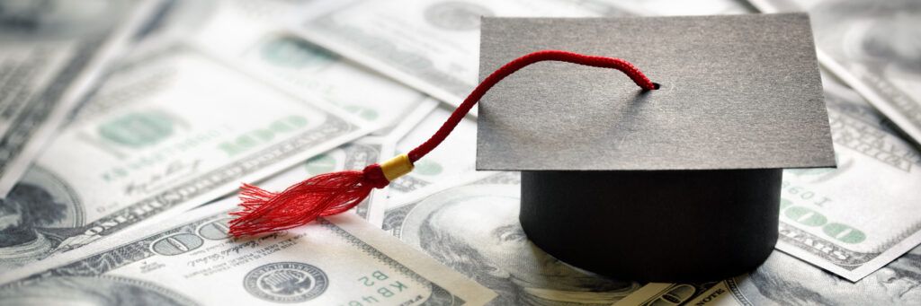 A graduation cap sitting on top of 100 dollar bills. 