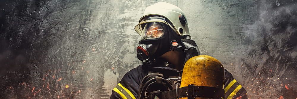 A firefighter with an oxygen mask on in front of a grey wall. 