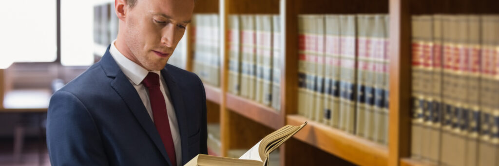 Man in blue suit reads casebook at law library.