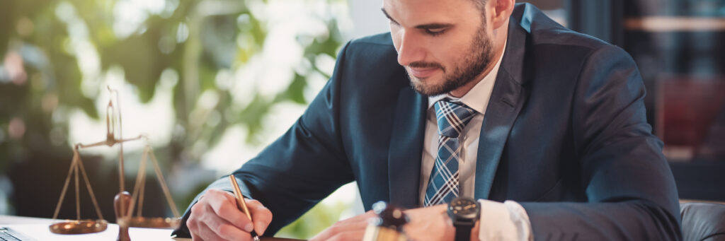 Attorney in blue jacket writes notes at his desk.