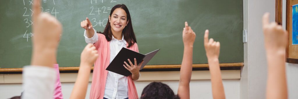 Teacher pointing at students raising their hands to respond to question.