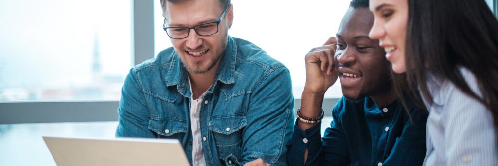 Teacher in denim jacket and two student review lesson on laptop.