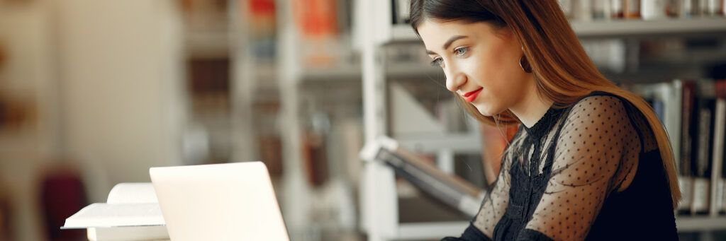 A young woman in a library focuses on working on her laptop.