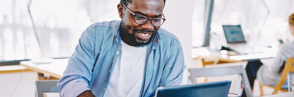 A man in a college classroom sits at his computer and smiles as he reads about the various career paths he can take by earning a psychology degree online.