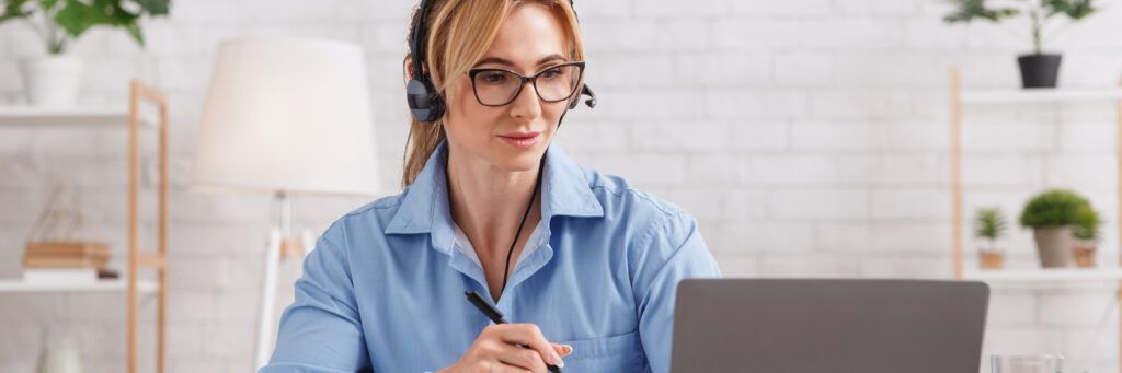 A woman in office clothes works on her laptop while wearing headphones.