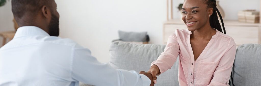 A smiling young woman shakes hands with her therapist as she sits on a sofa.