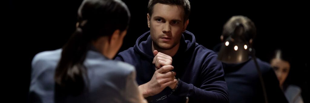 A woman questions a nervous-looking man in an interrogation room.