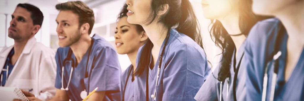 Multiple students in scrubs listen to their instructor while earning one of the top online public health degrees.