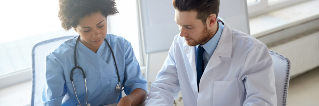 A woman in scrubs and a man in a lab coat are looking down, considering their options for a Doctor of Public health degree.