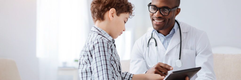 A man in a lab coat smiles while evaluating a boy after graduating with a PhD in Public Health Online.