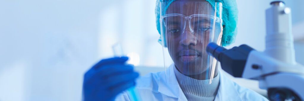 A man in scrubs and protective goggles examines a sample while earning a PhD in epidemiology online.