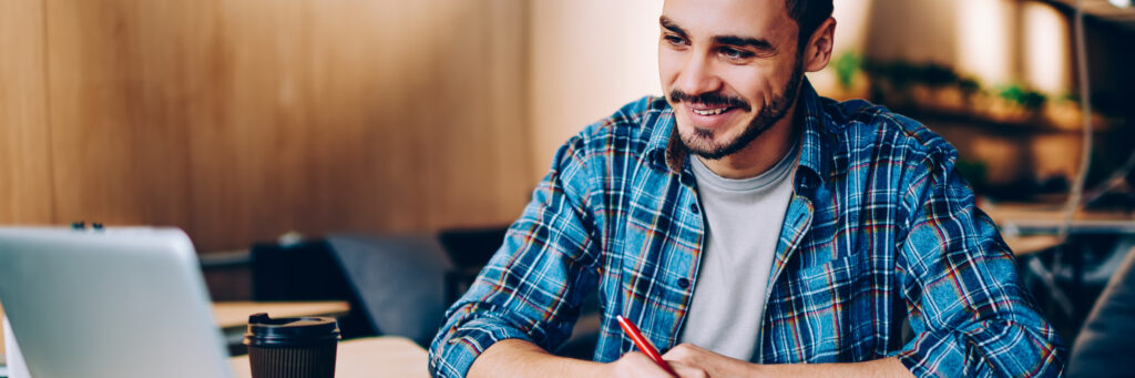 A man smiles and looks at his laptop screen while earning a doctor of social work online.