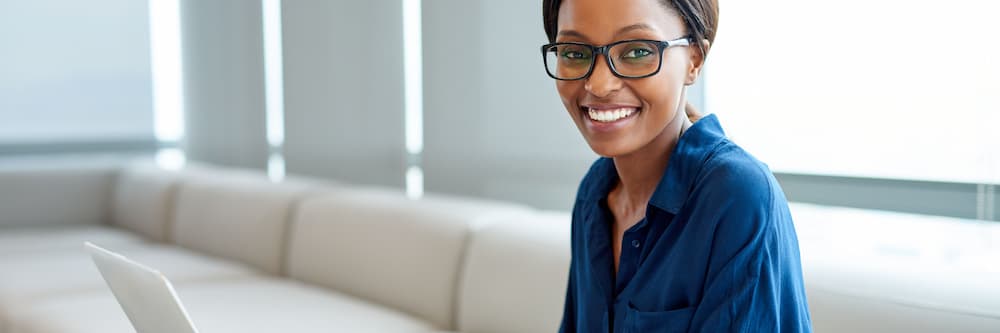 A woman in glasses sits at a laptop and smiles confidently into the camera while learning what you can do with a public administration degree.