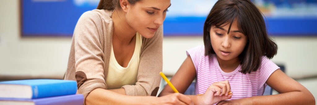 A student teacher helping an elementary schooler with their homework.