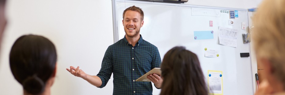 Smiling man in blue shirt with tablet teaches class.